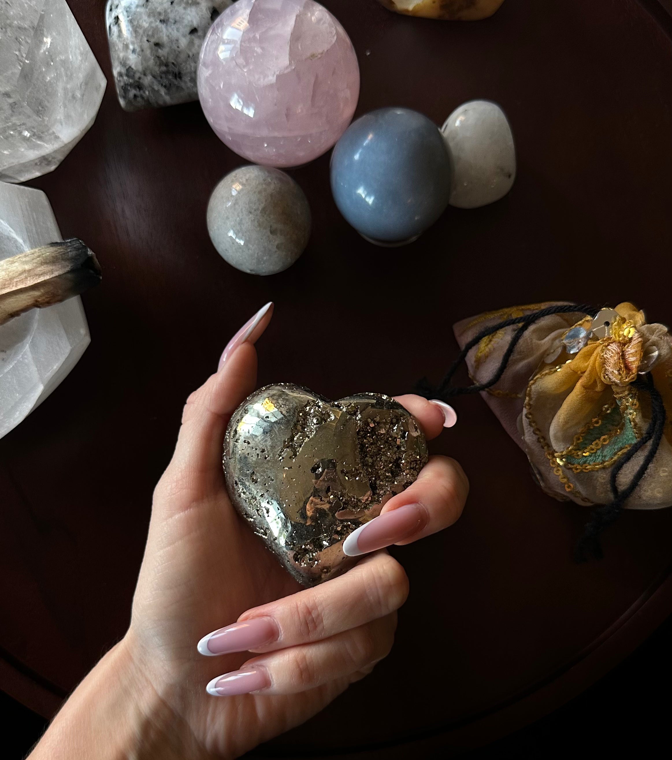 Hand holding a heart-shaped Pyrite crystal with other crystals on a dark surface