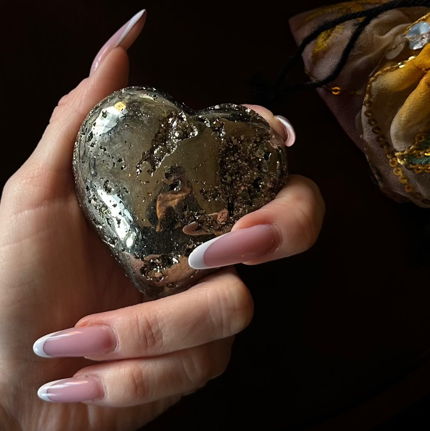 Hand holding a pyrite heart against a dark background beautiful nails and hands